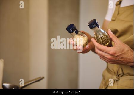 Die Hände des Küchenchefs halten zwei Glasflaschen mit Gewürzen zum Würzen während des Abendessens Stockfoto