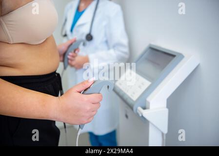 Ein Heilpraktiker hilft fettleibigen jungen Frauen mit einem Körperzusammensetzungstest mit fortschrittlichen Geräten. Stockfoto