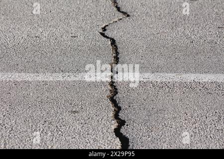 Großer Riss auf der öffentlichen asphaltierten Asphaltstraße, der nach einem großen Erdbeben auftauchte und darauf wartete, an warmen sonnigen Wintertagen gefüllt und repariert zu werden Stockfoto