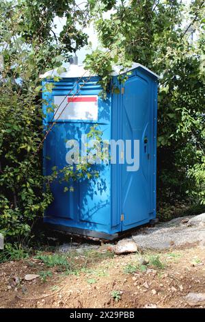 Neue tragbare Unisex-blaue Toilette mit weißer Oberseite oder tragbare Chemikalientoilette auf einem stabilen Kunststofffundament auf Holzpalette Stockfoto