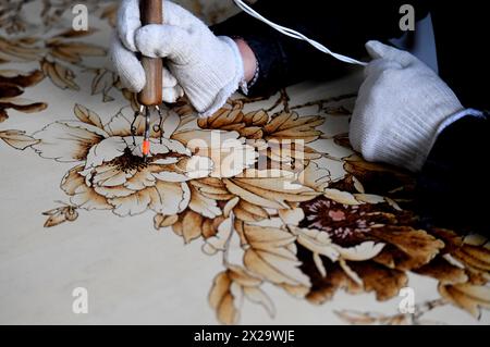 (240421) -- NANYANG, 21. April 2024 (Xinhua) -- Li Zhe macht eine Holzpyrographie in einem Studio der Nanyang Pyrography Factory in Nanyang City, Zentralchinas Provinz Henan, 15. März 2024. Die Nanyang Pyrographie, eine traditionelle chinesische Kunst, die aus der westlichen Han-Dynastie (206 v. Chr.–25 n. Chr.) stammt, hat eine über 2.000-jährige Geschichte. Das Handwerk verwendet Werkzeuge mit hoher Temperatur, um Muster auf karbonisierbaren Materialien zu zeichnen, erzeugt visuelle Effekte, die an traditionelle chinesische Gemälde erinnern. Es wurde 2021 als immaterielles Kulturerbe auf nationaler Ebene aufgeführt. Li Zhe, 54 Jahre alt, ist ein Erben auf Provinzebene Stockfoto