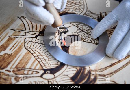 (240421) -- NANYANG, 21. April 2024 (Xinhua) -- Li Zhe macht eine Holzpyrographie in einem Studio der Nanyang Pyrography Factory in Nanyang City, Zentralchinas Provinz Henan, 15. März 2024. Die Nanyang Pyrographie, eine traditionelle chinesische Kunst, die aus der westlichen Han-Dynastie (206 v. Chr.–25 n. Chr.) stammt, hat eine über 2.000-jährige Geschichte. Das Handwerk verwendet Werkzeuge mit hoher Temperatur, um Muster auf karbonisierbaren Materialien zu zeichnen, erzeugt visuelle Effekte, die an traditionelle chinesische Gemälde erinnern. Es wurde 2021 als immaterielles Kulturerbe auf nationaler Ebene aufgeführt. Li Zhe, 54 Jahre alt, ist ein Erben auf Provinzebene Stockfoto