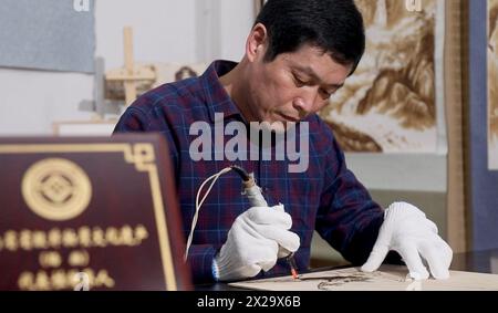 (240421) -- NANYANG, 21. April 2024 (Xinhua) -- dieses undatierte Foto zeigt Li Zhe, der eine Holzpyrographie in einem Studio der Nanyang Pyrography Factory in Nanyang City, Zentralchinas Provinz Henan, macht. Die Nanyang Pyrographie, eine traditionelle chinesische Kunst, die aus der westlichen Han-Dynastie (206 v. Chr.–25 n. Chr.) stammt, hat eine über 2.000-jährige Geschichte. Das Handwerk verwendet Werkzeuge mit hoher Temperatur, um Muster auf karbonisierbaren Materialien zu zeichnen, erzeugt visuelle Effekte, die an traditionelle chinesische Gemälde erinnern. Es wurde 2021 als immaterielles Kulturerbe auf nationaler Ebene aufgeführt. Li Zhe, 54, ist ein inh auf Provinzebene Stockfoto