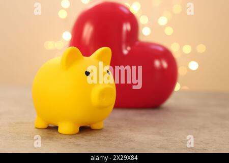 Gelbe Schweinebank und Keramikherz auf grauem Tisch vor verschwommenem Licht Stockfoto