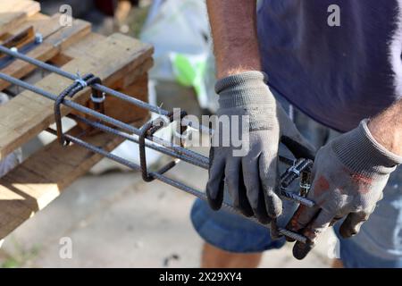 Der professionelle Baumeister arbeitet mit Bewehrungsstahl. Bauarbeiten im Gange. Mann in grauen Handschuhen hält Metallrahmen. Stockfoto