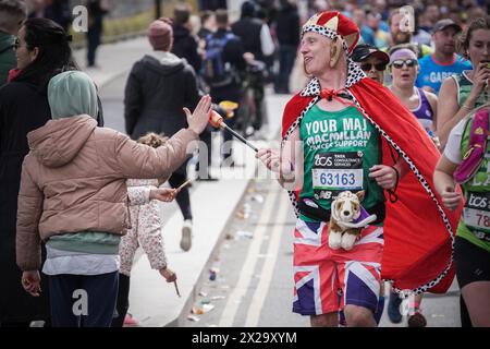 London, Großbritannien. April 2024. Läufer verkleidet als König Charles. Der London Marathon führt die Evelyn Street in Deptford in South East London hinunter, die 13 km lange Strecke der 26,2 km langen Strecke, auf der Läufer von Einheimischen begrüßt und angefeuert werden. Guy Corbishley/Alamy Live News Stockfoto