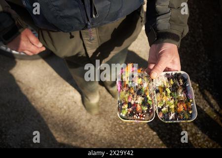 Ein Fischer, grün gekleidet, zeigt seine Kiste mit Fischfliegen. Stockfoto