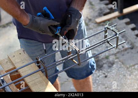 Der professionelle Baumeister arbeitet mit Bewehrungsstahl. Bauarbeiten im Gange. Mann in grauen Handschuhen hält Metallrahmen. Stockfoto