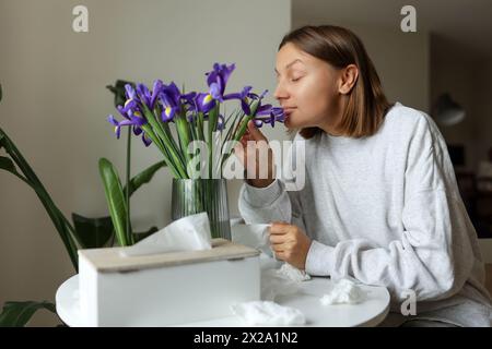 Saisonale Allergikerfrei. Junge Frau schnüffelt von Irisblumen, genießt den Geruch ohne laufende Nase, Jucken oder Husten saisonale Symptome in gemütlichem Zuhause. Gir Stockfoto