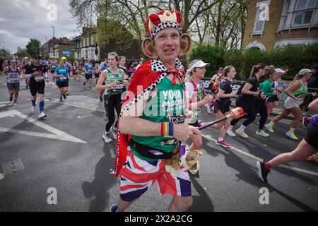 London, Großbritannien. April 2024. Läufer verkleidet als König Charles. Der London Marathon führt die Evelyn Street in Deptford in South East London hinunter, die 13 km lange Strecke der 26,2 km langen Strecke, auf der Läufer von Einheimischen begrüßt und angefeuert werden. Guy Corbishley/Alamy Live News Stockfoto