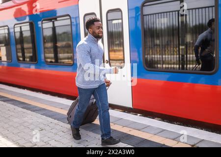 Mann, der mit Koffer zu einem ausfahrenden Zug am Bahnhof läuft. Stockfoto