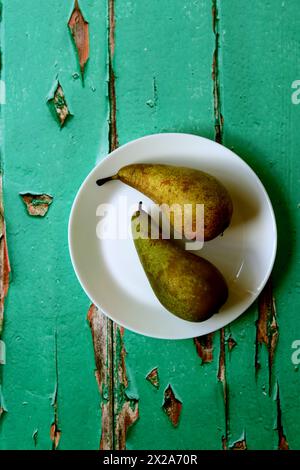 Zwei grüne Birnen auf einem weißen Teller. Foto von oben von einem alten Holztisch. Konzept für gesunde Ernährung. Stockfoto