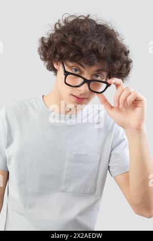 Lächelnd und gut aussehend, trägt der junge Mann eine Brille. Er schaut in die Kamera mit seinen blauen Augen, ein Mannporträt mit Brille isoliert gegen ein graues B Stockfoto