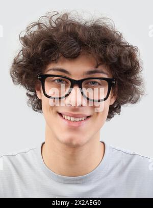 Lächelnd und gut aussehend, trägt der junge Mann eine Brille. Er schaut in die Kamera mit seinen blauen Augen, ein Mannporträt mit Brille isoliert gegen ein graues B Stockfoto
