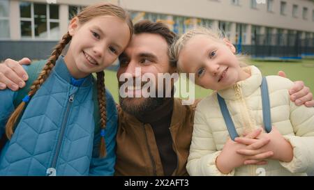 Vater und zwei Töchter schauen in die Kamera lächelnd lachend glückliche Familieneltern lieben Freude Grundschüler Schülerinnen Schüler Nachkommen Stockfoto