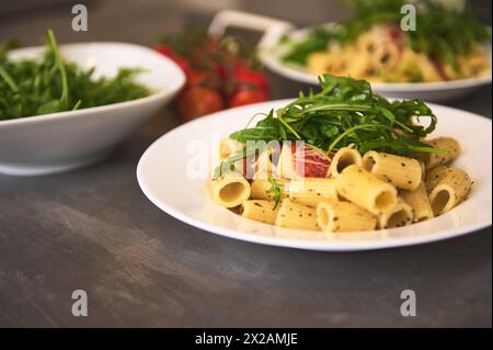 Hausgemachte italienische Penne-Pasta mit Sauce, Tomaten, Rucola, Basilikum und Parmesan. Traditionelle italienische Küche. Serviert auf einem dunklen Tisch mit einer Kleie Stockfoto