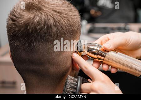 Friseur rasiert männliche Kundenbehaarung mit Trimmer im Friseur. Der Friseur rasiert einen Tempel Stockfoto