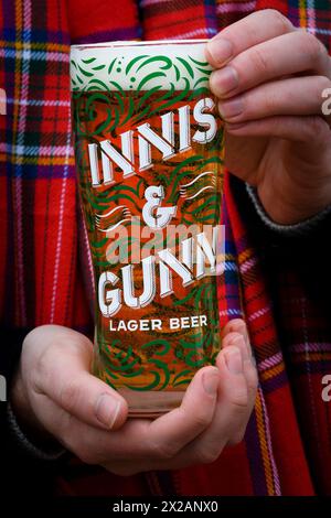 Eine Hand hält ein Pint Innis and Gunn Lager in einem Markenglas vor einem Tartan-Hintergrund, Schottland, UK Stockfoto