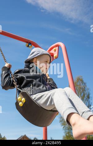 Kleiner Junge schwingt auf einer Schaukel vor blauem Himmel Hintergrund, niedriger Blickwinkel. Stockfoto