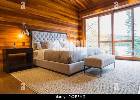 King size Bett mit grauen gepolsterten panel Kopfteil, osmanischen und Holz- Ende Tabellen im Hauptschlafzimmer mit grauen Nuancen Wolldecke und Ipe holz Boden, Innen, l Stockfoto