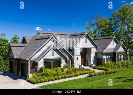 Zeitgenössische Naturstein und braun gebeiztes Holz und Zedernschindeln bekleidet luxuriöse Bungalow-Stil Hausfassade im Sommer, Quebec, Kanada, Nordamerika Stockfoto