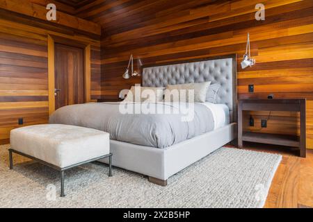 King size Bett mit grauen gepolsterten panel Kopfteil, osmanischen und Holz- Ende Tabellen im Hauptschlafzimmer mit grauen Nuancen Wolldecke und Ipe holz Boden, Innen, l Stockfoto