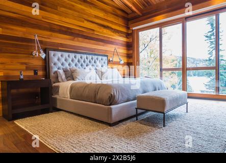 King size Bett mit grauen gepolsterten panel Kopfteil, osmanischen und Holz- Ende Tabellen im Hauptschlafzimmer mit grauen Nuancen Wolldecke und Ipe holz Boden, Innen, l Stockfoto