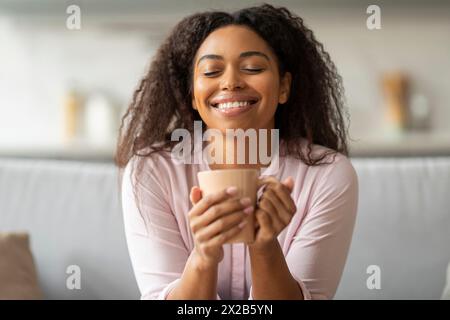 Glückliche Frau schlürft Kaffee auf der Couch Stockfoto