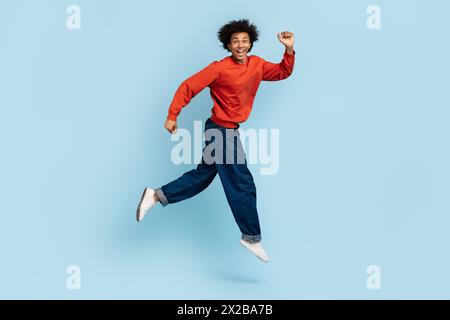 Überschwänglicher junger Mann, der auf blauem Hintergrund läuft und lächelt Stockfoto