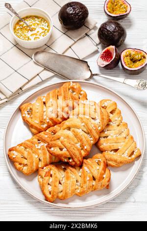 Passionsfrucht Turnovers süße Kuchen auf Teller auf weißem Holztisch mit Kuchenschaufel, frische Passionsfrüchte, vertikale Ansicht von oben Stockfoto