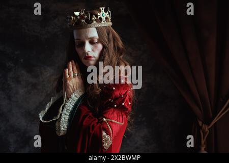 Mittelalterliche Königin in rotem Kleid mit Kronenbeten auf dunkelgrauem Hintergrund. Stockfoto