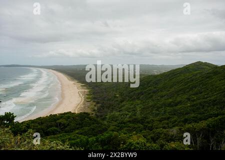 Ein herrlicher Panoramablick fängt die ruhige Schönheit des grünen, gesäumten Strandes von Byron Bay an einem bewölkten Tag ein, von der Bergspitze aus gesehen Stockfoto