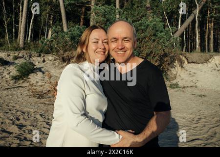 Ein Mann und eine Frau umarmen sich liebevoll an einem Sandstrand, mit dem Meer im Hintergrund. Stockfoto