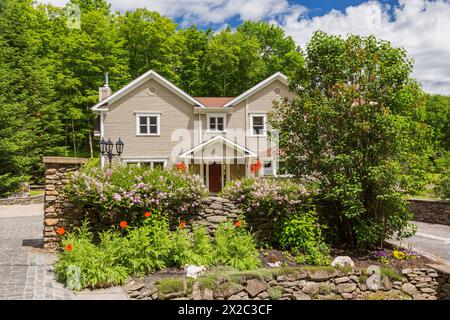 Braun mit weißen Zierleisten, zeitgenössische viktorianische Landhausfassade im 1990er-Jahre-Stil mit roten Begonien in hängenden Körben, Natursteinwand und roten Papavers. Stockfoto