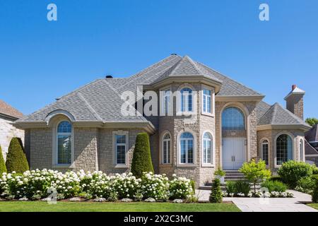 Beigefarbener Stein mit weißer Zierleiste luxuriöse zweistöckige Hausfassade mit landschaftlich gestaltetem Vorhof im Sommer. Stockfoto