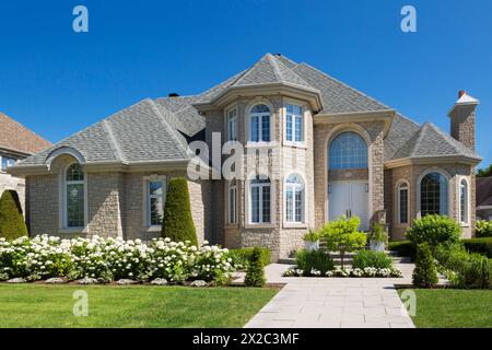 Beigefarbener Stein mit weißer Zierleiste luxuriöse zweistöckige Hausfassade mit landschaftlich gestaltetem Vorhof im Sommer. Stockfoto
