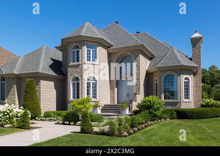 Beigefarbener Stein mit weißer Zierleiste luxuriöse zweistöckige Hausfassade mit landschaftlich gestaltetem Vorhof im Sommer. Stockfoto