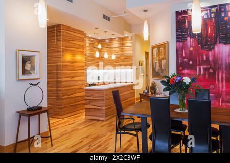 Gumwood-Schränke und Insel mit reinweißem Quarzarbeitsplatz in der Küche und Palisander-Tisch mit schwarzen Ledersesseln mit hoher Rückenlehne im Esszimmer. Stockfoto