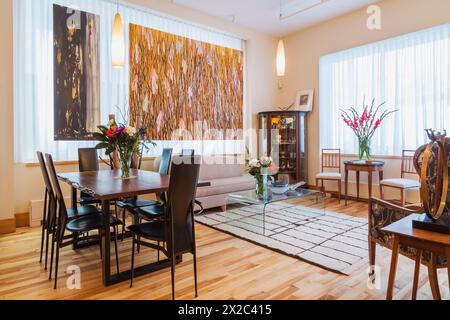 Palisander-Tisch mit schwarzen Ledersesseln mit hoher Rückenlehne im Esszimmer/Wohnbereich mit gepolstertem wohnbereich, Couchtisch aus klarem Glas in der Wohnung. Stockfoto