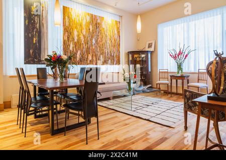 Palisander-Tisch mit schwarzen Ledersesseln mit hoher Rückenlehne im Esszimmer/Wohnbereich mit gepolstertem wohnbereich, Couchtisch aus klarem Glas in der Wohnung. Stockfoto