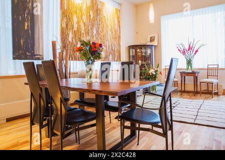 Palisander-Tisch mit schwarzen Ledersesseln mit hoher Rückenlehne im Esszimmer/Wohnbereich mit gepolstertem wohnbereich, Couchtisch aus klarem Glas in der Wohnung. Stockfoto