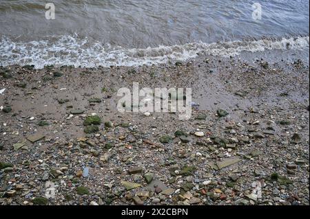 Blick hinunter auf kleine Wellen, die bei Ebbe auf Felsen und Steinen am Flussufer brechen Stockfoto