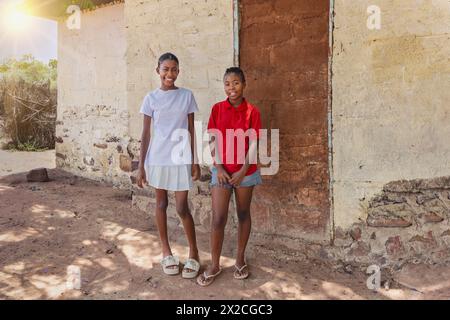 Zwei lächelnde afrikanische Teenagermädchen vor dem Haus in der armen Gemeinde, informelle Siedlung Stockfoto