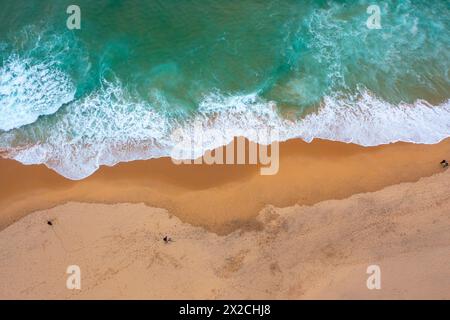 Drohnenansicht mit wunderschönen, nahtlosen Aufnahmen, während türkisfarbene Wellen an der sandigen Küste aufbrechen. Luftaufnahme des goldenen Strandes, der tiefes blaues Ozeanwasser und schaumige Wellen trifft Stockfoto