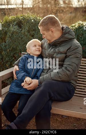 Herbstliche Familienzusammenhänge: Vater, 40 Jahre alt, und Sohn - wunderschöner 8-jähriger Junge, im Park sitzend. Stockfoto