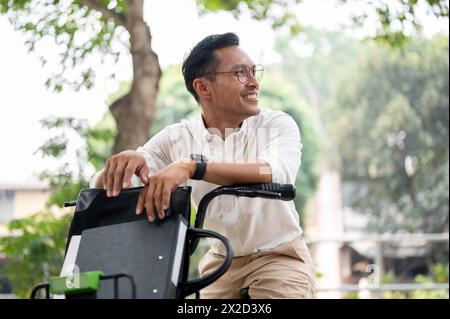 Ein gutaussehender, glücklicher asiatischer Geschäftsmann der Millennials ist auf einem Fahrrad im Park und fährt morgens mit dem Fahrrad zur Arbeit. Geschäftsleute und Transportmittel Stockfoto