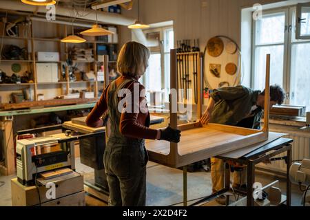 Ein interessiertes Paar arbeitet in einer Tischlerei und macht zusammen einen handgemachten Tisch. Kleines Holzgeschäft. Stockfoto