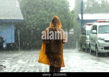 Ein Mann läuft im Regen mit gelbem Regenmantel in Bogor, West Java, Indonesien, am 31. März 2024 Stockfoto