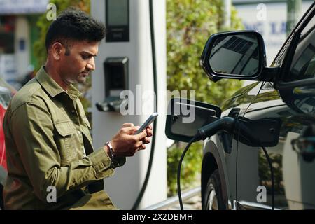 Ein runzelnder Mann, der auf das Aufladen seines Elektroautos wartet Stockfoto