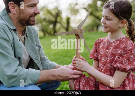 Vater unterrichtet Tochter über erneuerbare Windenergie, nachhaltigen Lebensstil. Draußen im Park stehen, Windkraftanlage halten. Stockfoto